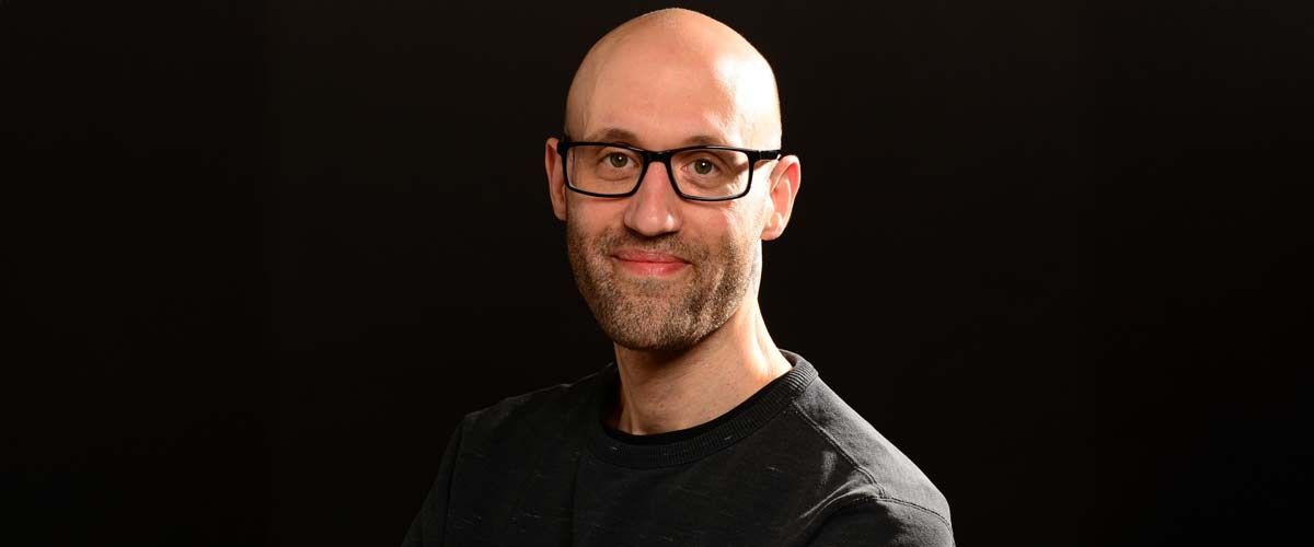 Alexander Peinelt freundlich lächelnd vor schwarzem Hintergrund